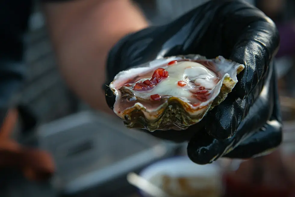 Hand holding a half shell oyster with seasoning